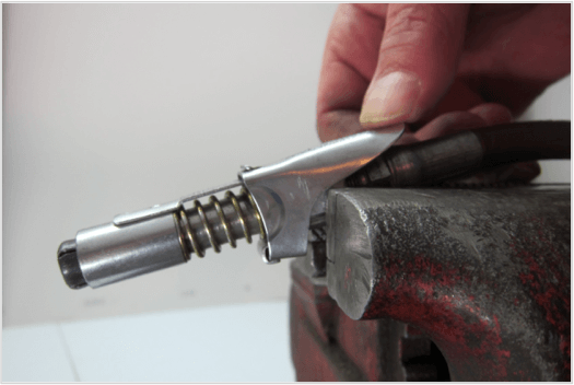 Close-up of a hand operating a LockNLube grease coupler, showcasing its steel jaws and threaded design on a workbench.