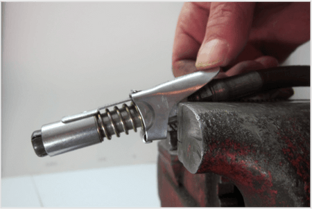 Close-up of a hand operating a LockNLube grease coupler, showcasing its steel jaws and threaded design on a workbench.