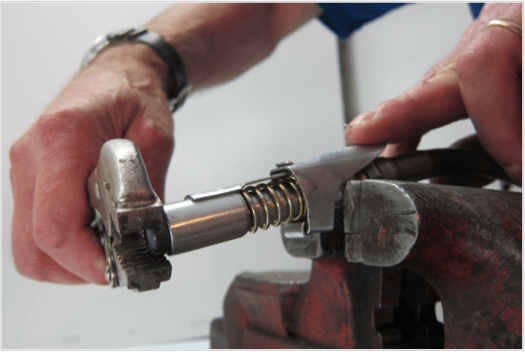 Close-up of hands using a tool to repair a LockNLube grease coupler in a vice.