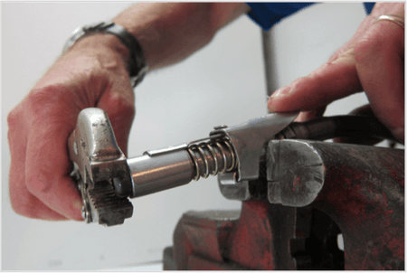 Close-up of hands using a tool to repair a LockNLube grease coupler in a vice.