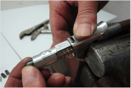 Close-up of hands holding a LockNLube® grease coupler, showcasing its internal components during a rebuild process.