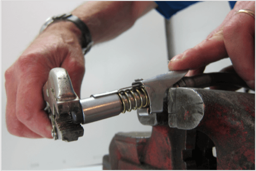 Hands using a wrench to adjust a LockNLube® Grease Coupler in a vice for maintenance and repair.