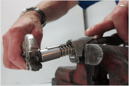 Hands using a wrench to adjust a LockNLube® Grease Coupler in a vice for maintenance and repair.