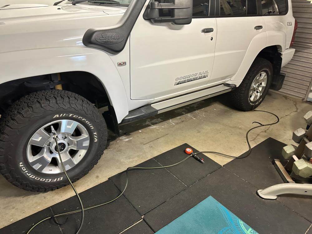 Locking air chuck in use on a white SUV's tire, showcasing secure connection with air hose for inflation.