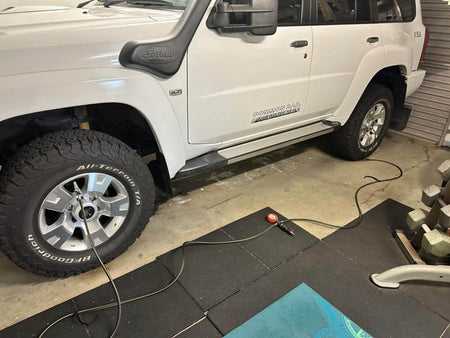 White SUV with large wheels connected to an air hose for tire inflation in a garage setting.