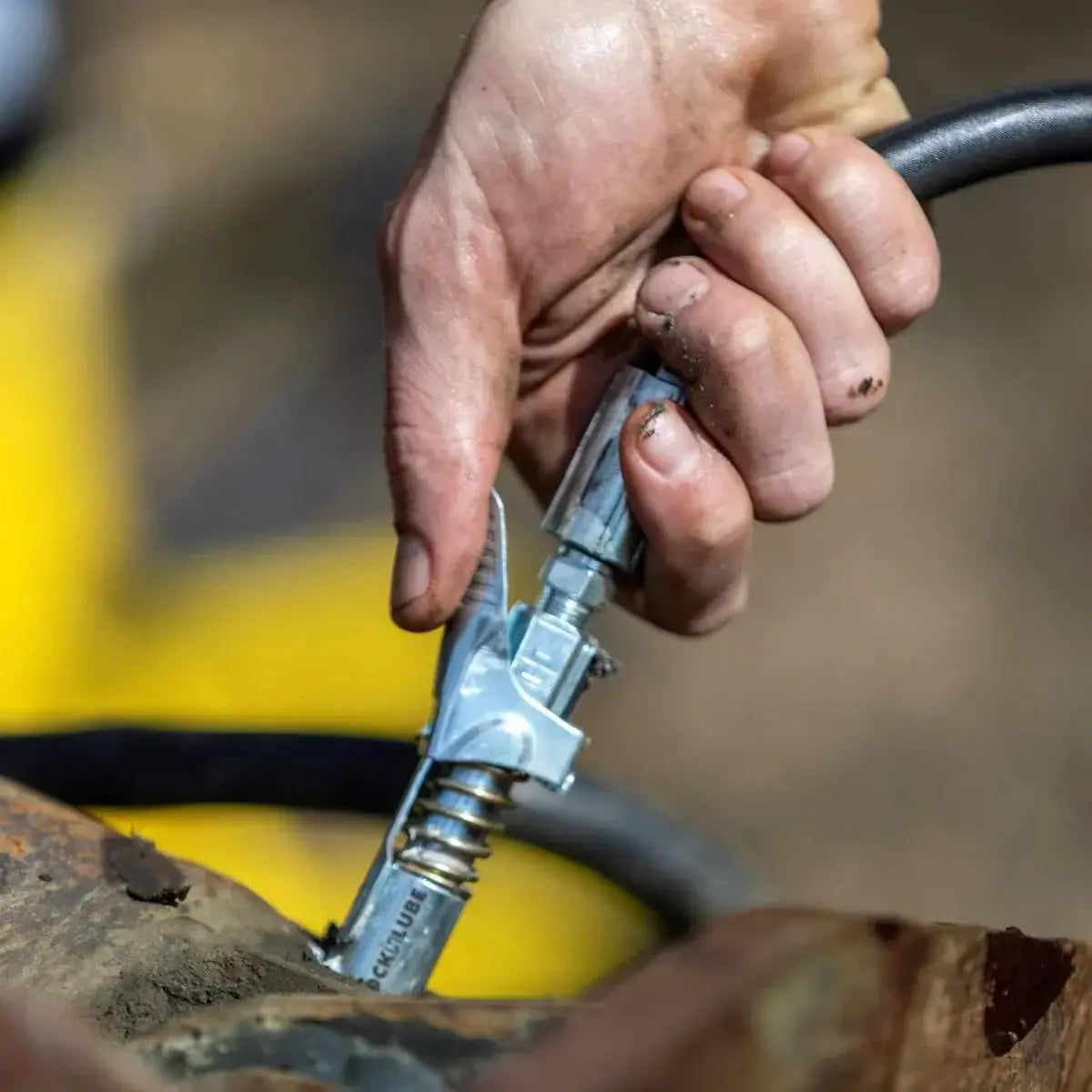 Hand using LOCKNLUBE® grease gun coupler on a machine, demonstrating easy connection and no leaks.