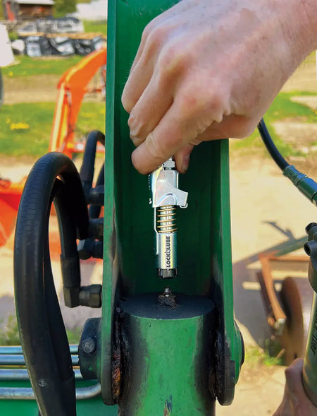 Person using LOCKNLUBE® grease gun coupler on machinery for efficient greasing without leaks or disconnect issues.