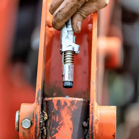 Hand using LockNLube grease gun coupler on heavy machinery for efficient greasing without leaks.