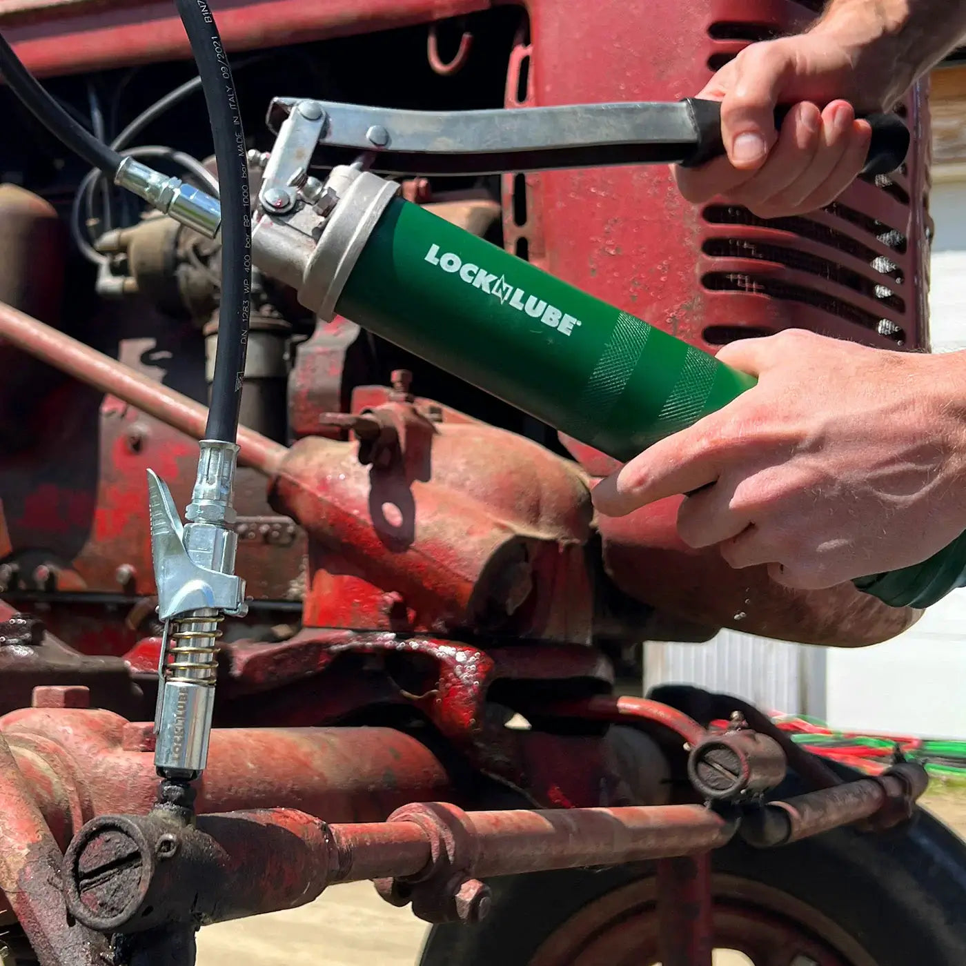 Person using LOCKNLUBE® grease gun coupler on machinery for efficient greasing without leaks or pressure issues.