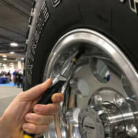 Hand using LOCKNFLATE® locking air chuck on a tire valve for secure inflation connection.