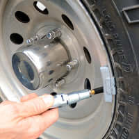 Hand using LOCKNFLATE® locking air chuck on a tire valve for secure, hands-free air inflating connection.